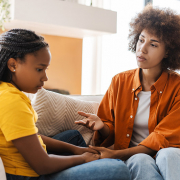 Mother holding her teenage daughter's hand and talking on the sofa