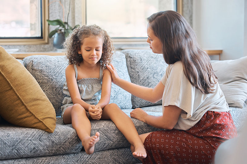 Young girl being comforted by her mum on the sofa