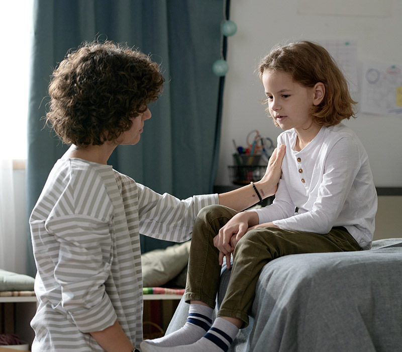 A mother talking to her child sitting on their bed