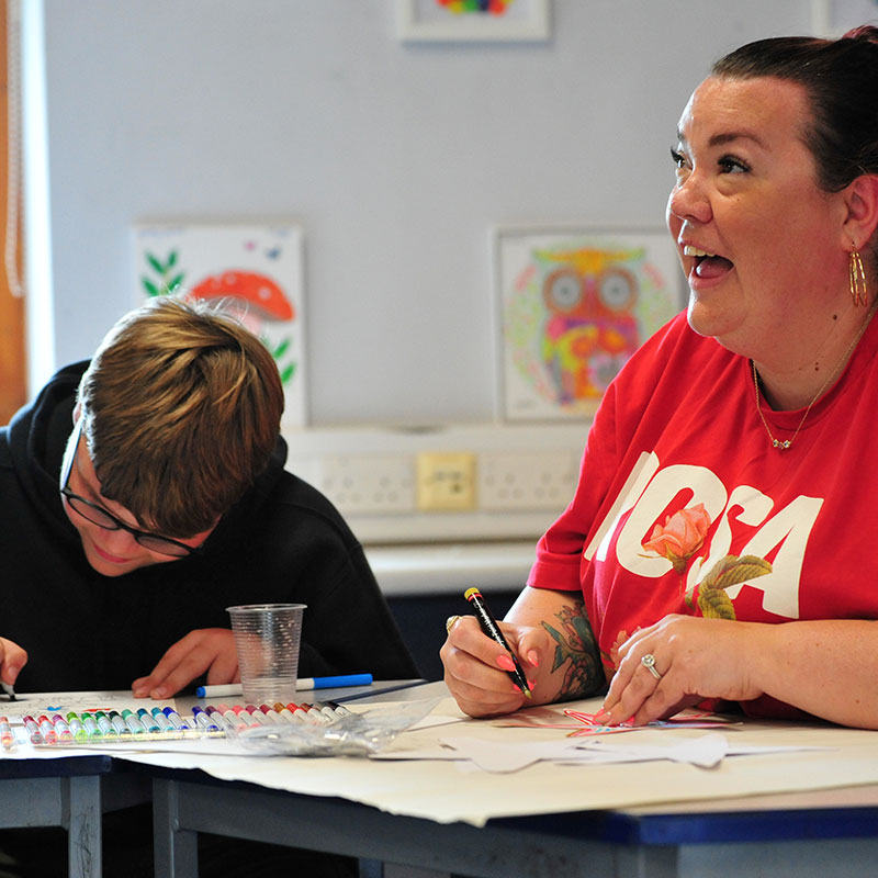 Woman and teenage boy drawing and smiling at a table