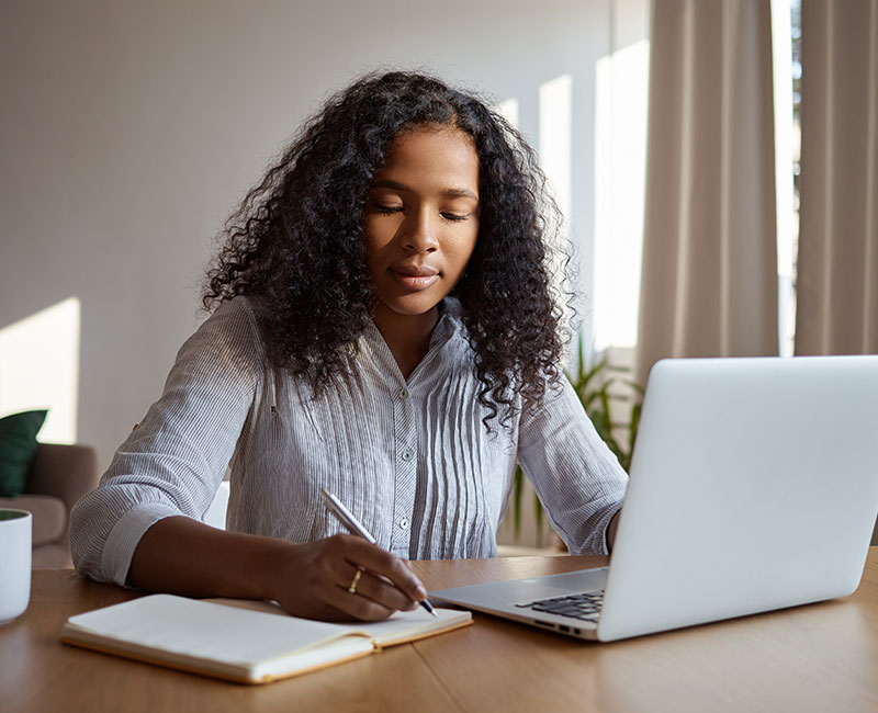 Woman at her laptop writing in a notepad